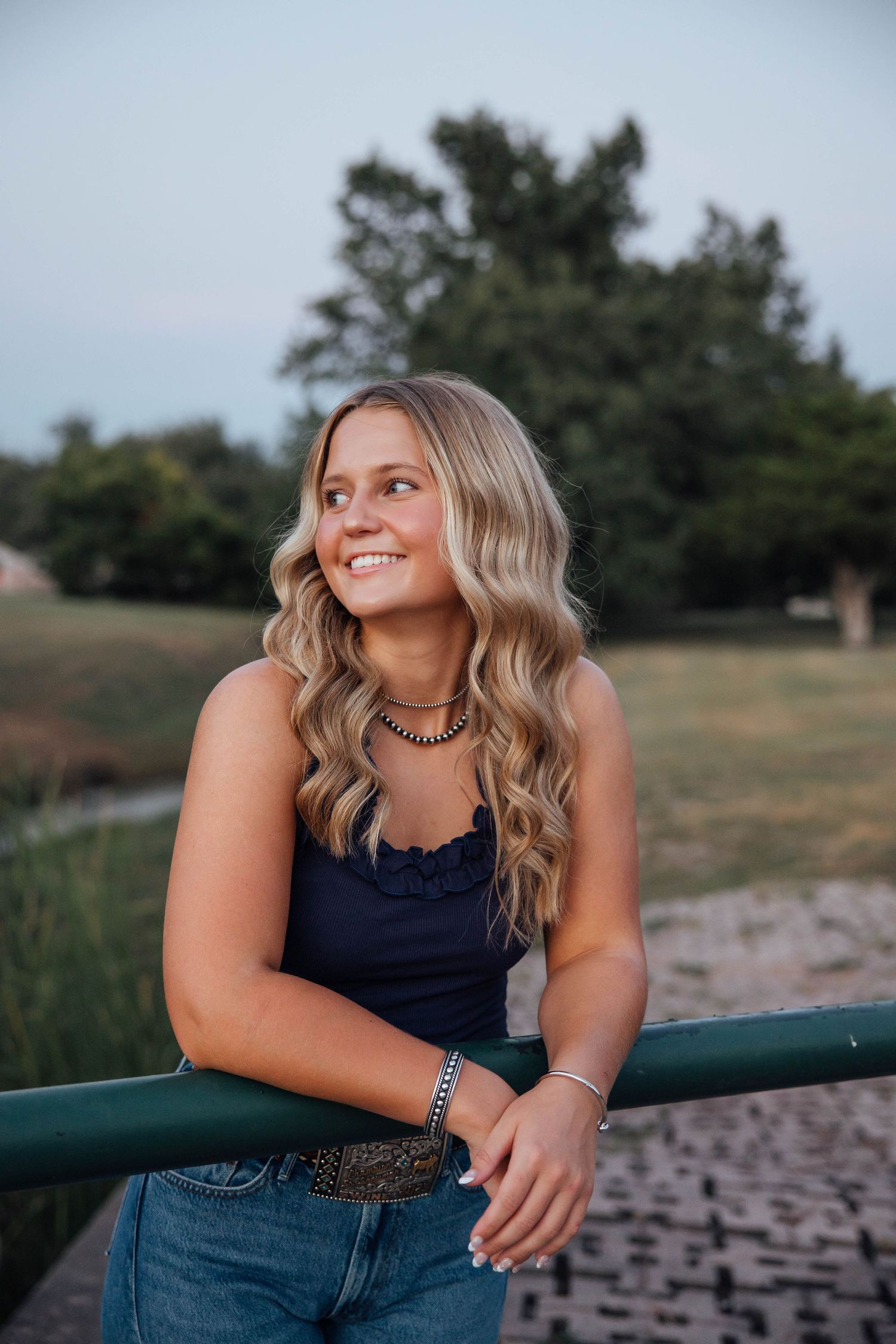Smiling blonde teen girl leaning on green railing outdoors at golden hour.