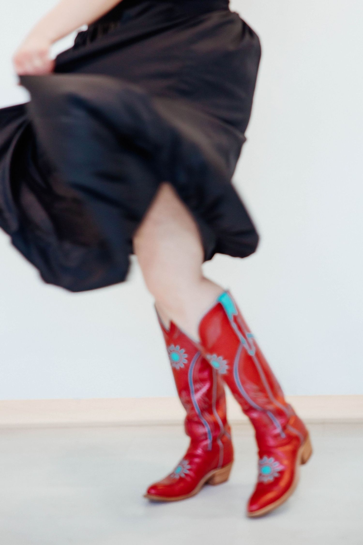 Woman dancing in black skirt and red cowboy boots with turquoise floral embroidery.