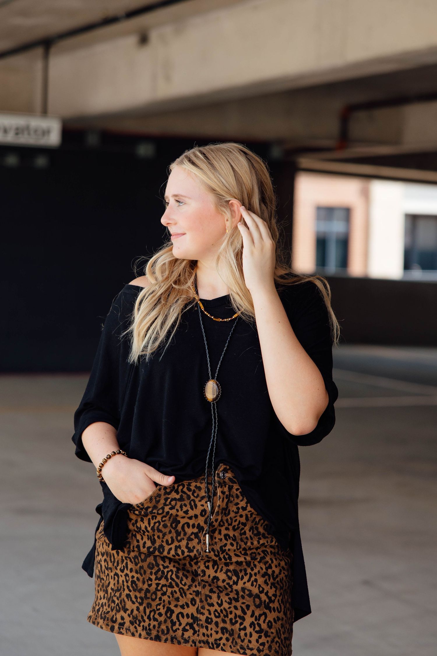 Blonde woman in black top and leopard print mini skirt poses in an urban parking garage setting.