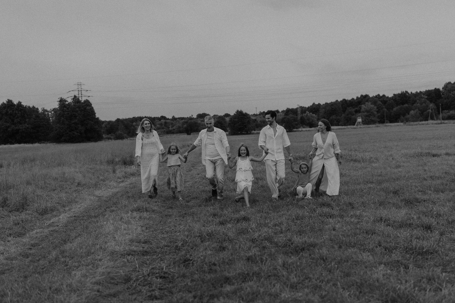 Black and white photo of a family holding hands walking through an open field at dusk.