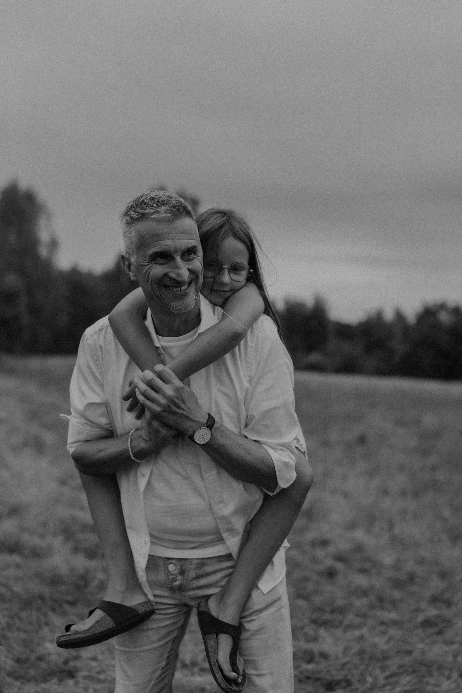 Black and white photo of a smiling man giving a young girl a piggyback ride in an open field.
