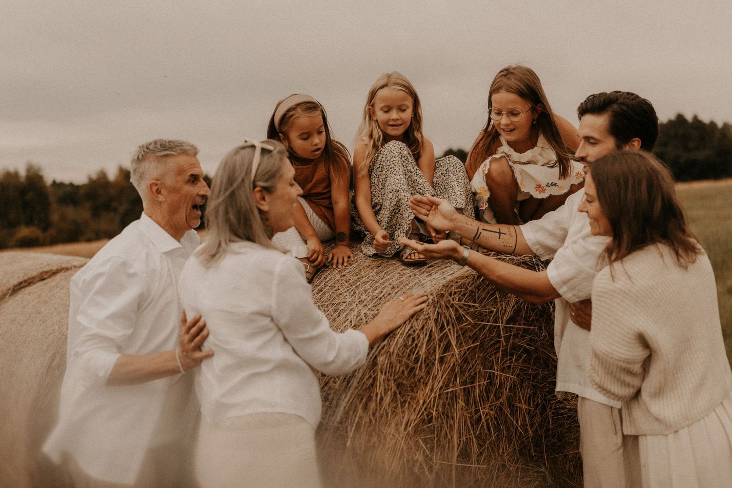 Multi-generational family laughing together around a hay bale in a field during an outdoor photo session.