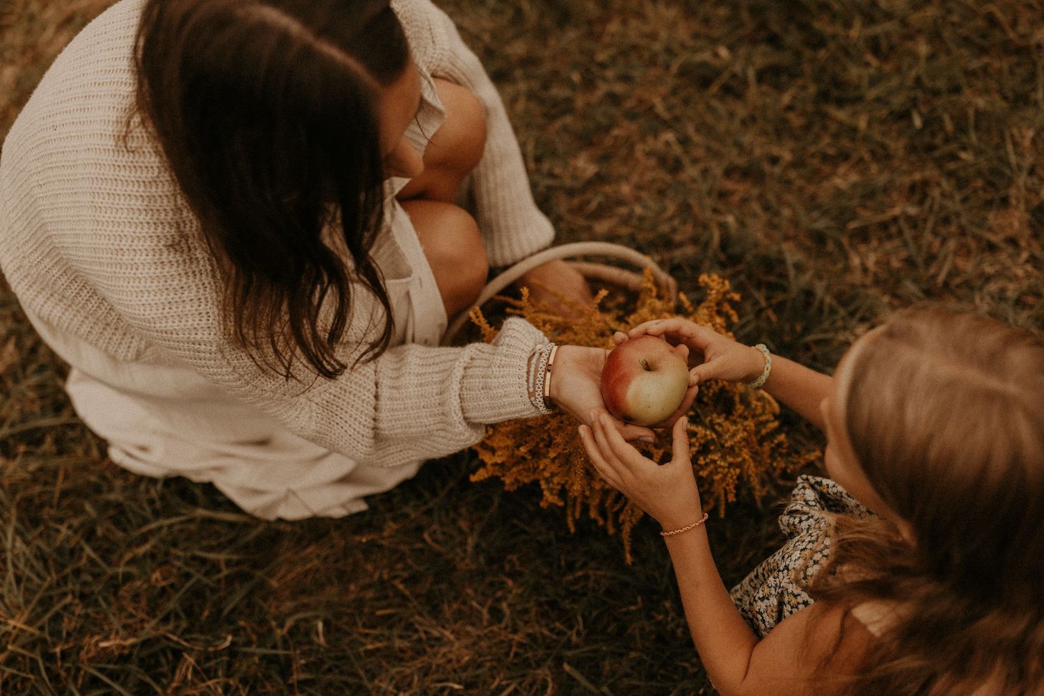 A mother and child share an apple during a cozy autumn outdoor picnic with a wicker basket filled with fall foliage.