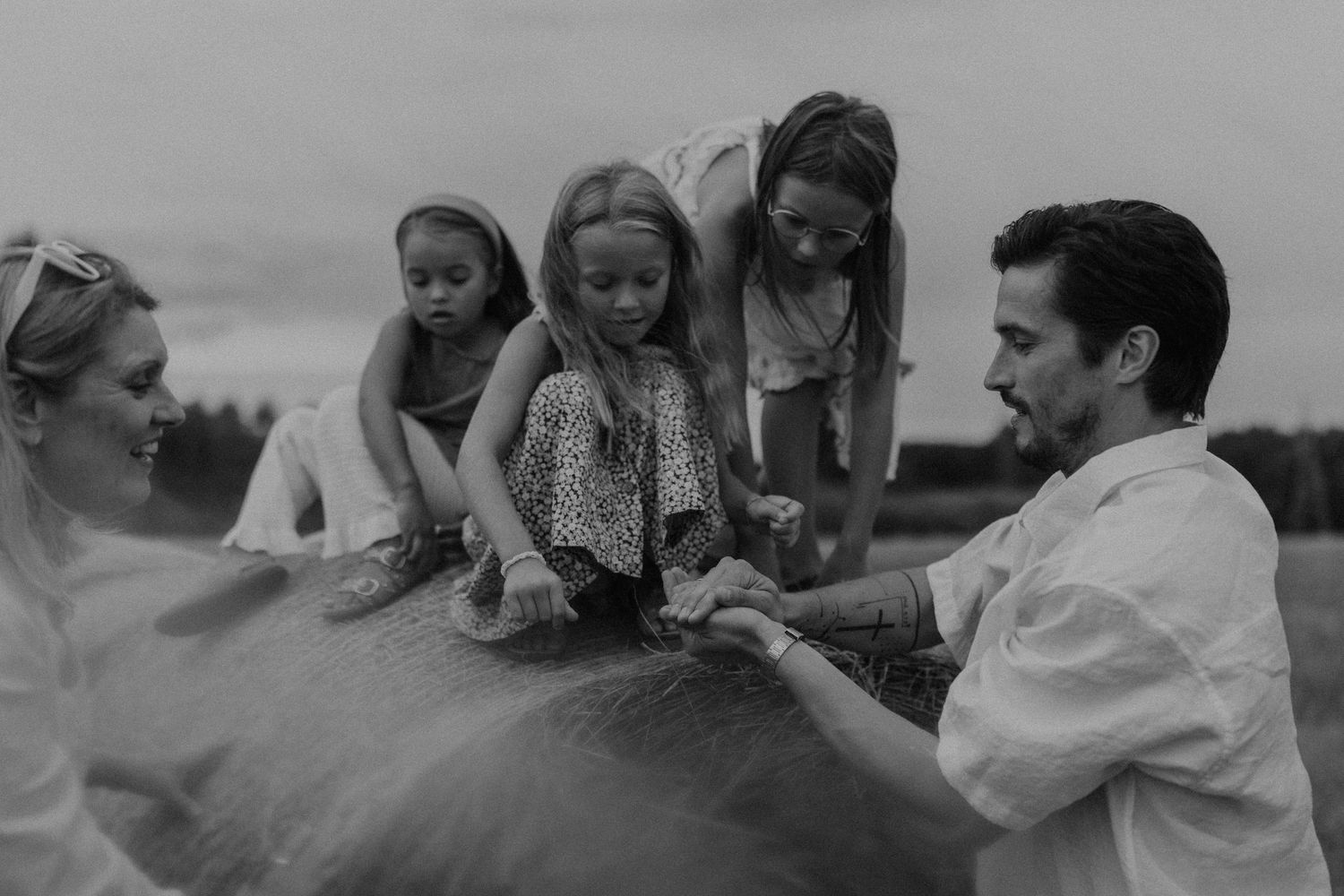 Black and white family photo of parents and children gathered around a horse in an outdoor field setting.
