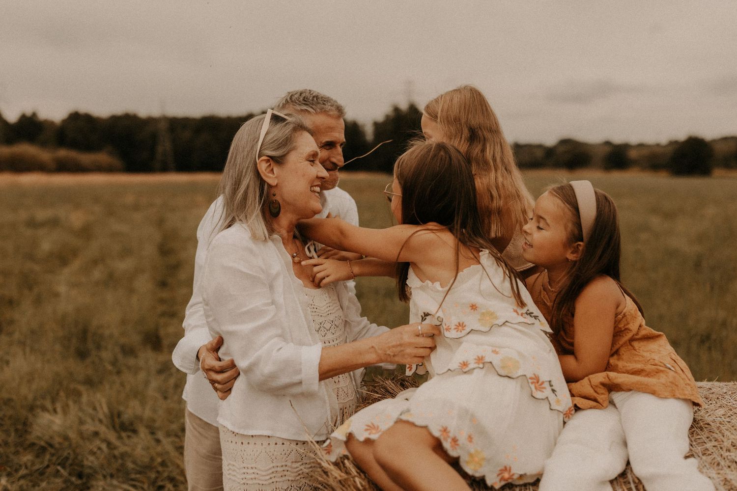 A joyful mother laughs with her three daughters in a golden field, sharing a warm and playful family moment outdoors.