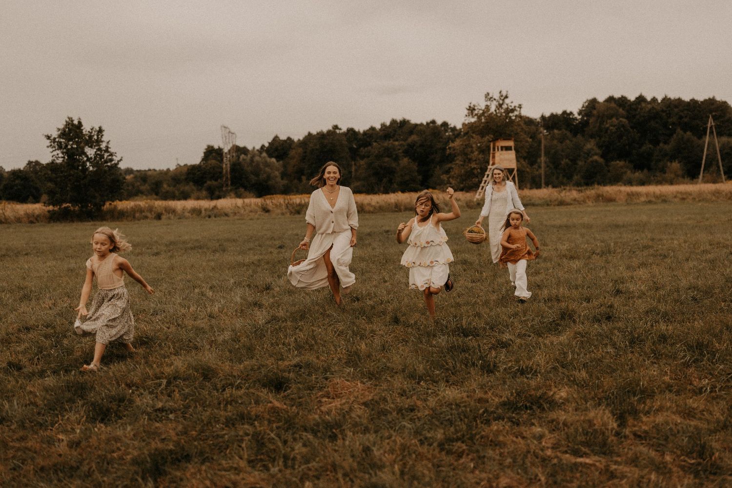 A joyful family with children running through a lush green field wearing white dresses on a cloudy day.