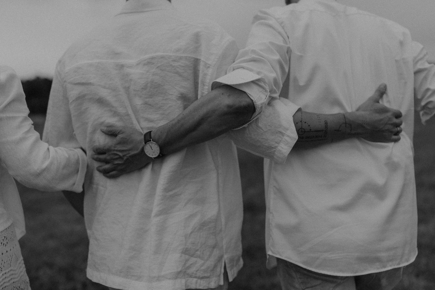 Three people in white shirts stand together with arms around each other in a black and white photo.