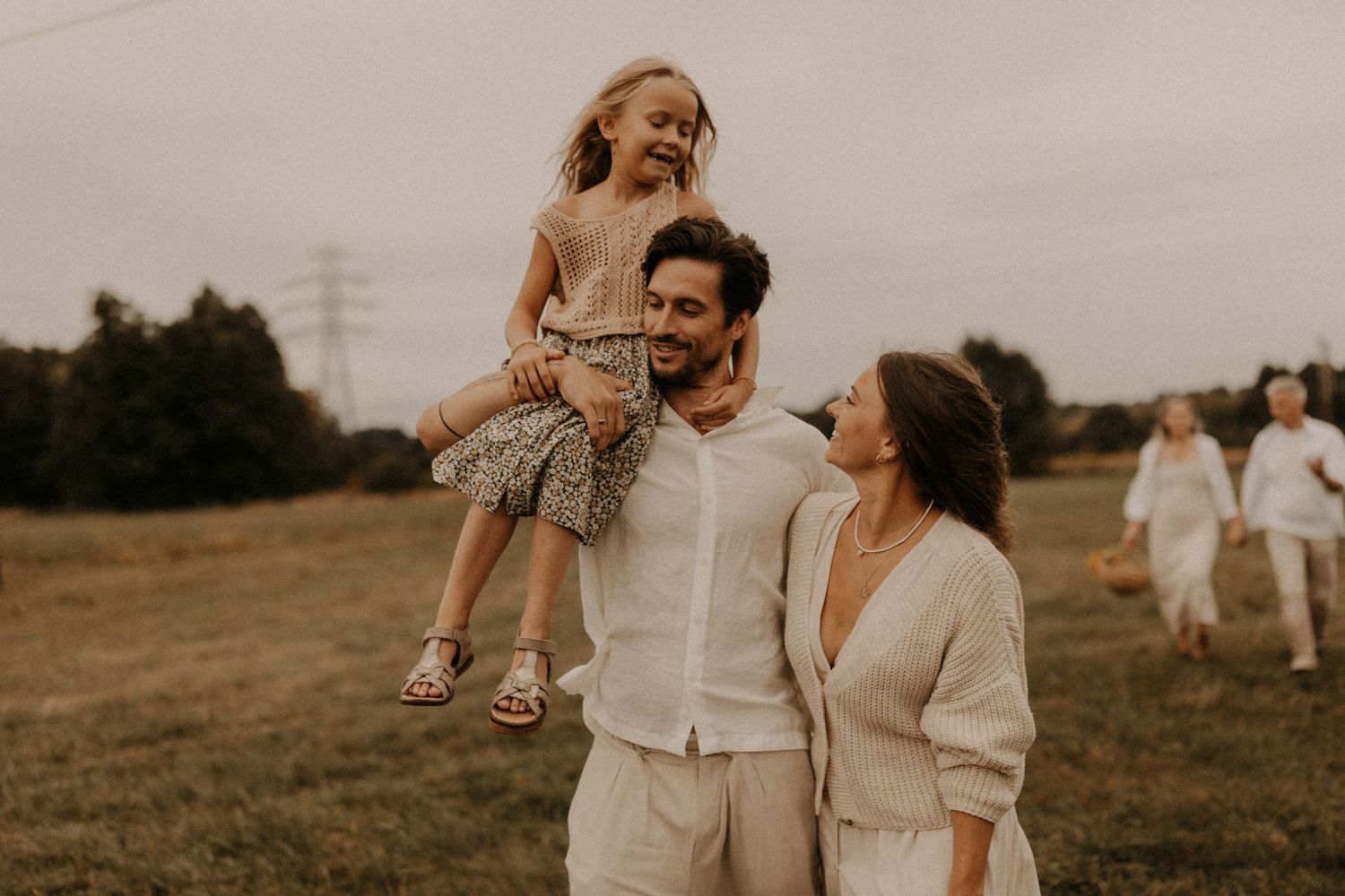 A happy family with a young girl on dad's shoulders walking in a green field during an outdoor photo session.