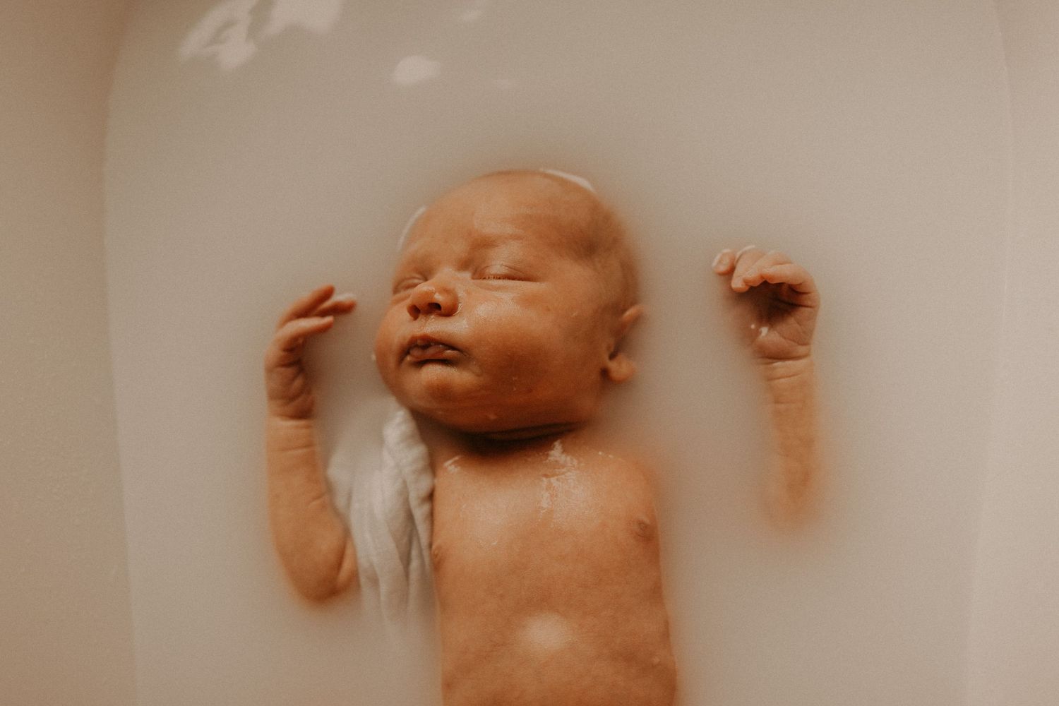 Newborn baby lying in warm water bath, eyes closed, tiny hands raised in relaxed pose. sesje zdjęciowe Rybnik, Wodzisław Śląski