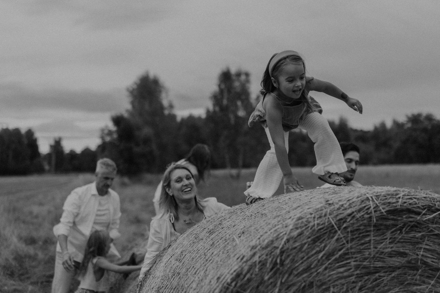 Black and white family photo with children playing on a hay bale in a rural field.