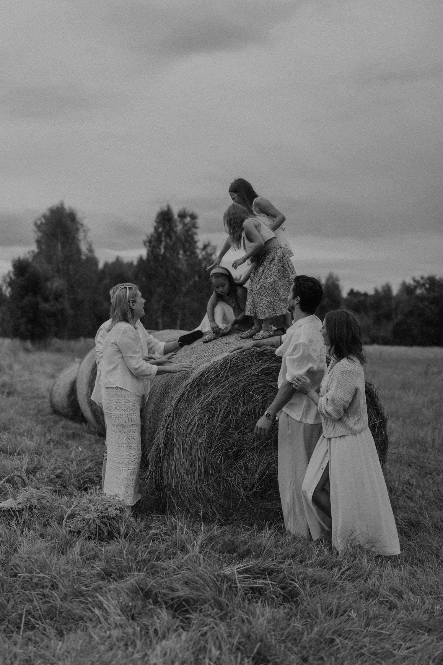 Black and white photo of a group of women in white dresses gathered around a large hay bale in a rural field.