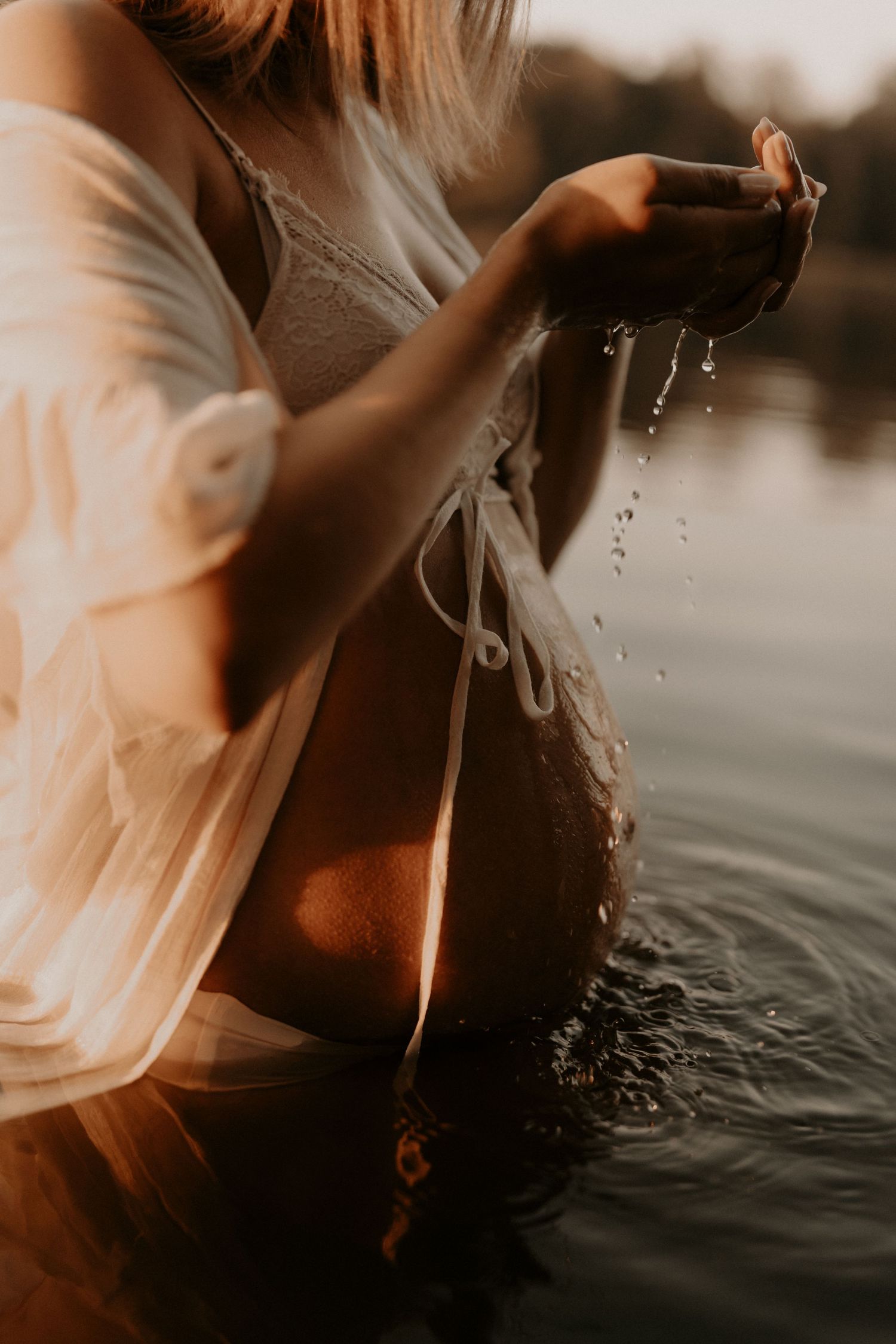 Golden hour maternity photo of a pregnant woman in white lingerie standing in a lake, water dripping. sesje zdjęciowe Rybnik, Wodzisław Śląs