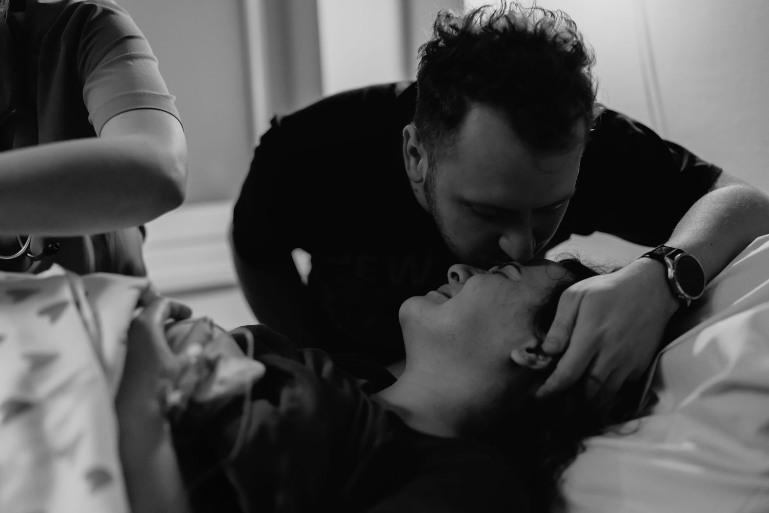 A tender moment as a man leans down to kiss a woman lying in a hospital bed after childbirth. reportaż porodu Rybnik, Wodzisław Śląski