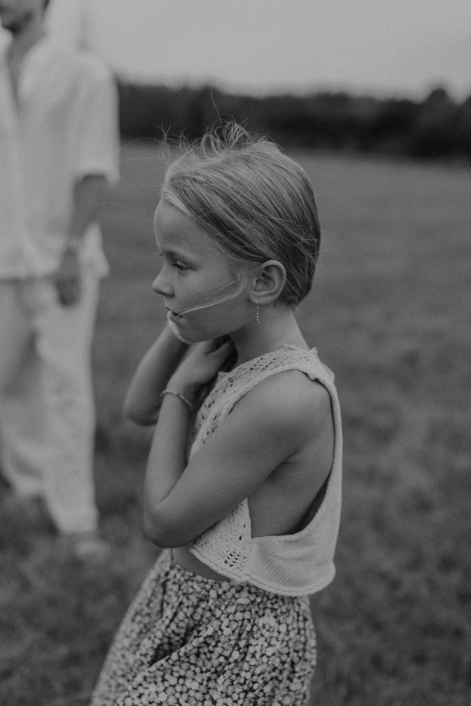 Black and white photo of a young girl in a floral skirt and sleeveless top standing in a field.