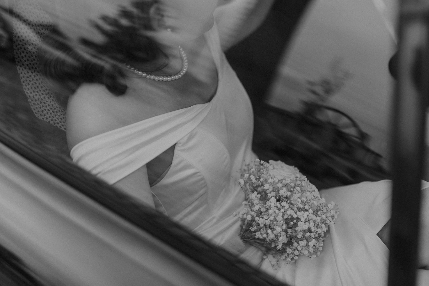 Black and white close-up of a bride in a wedding dress holding a bouquet, seen through a car window. sesje zdjęciowe Rybnik, Wodzisław Śląsk
