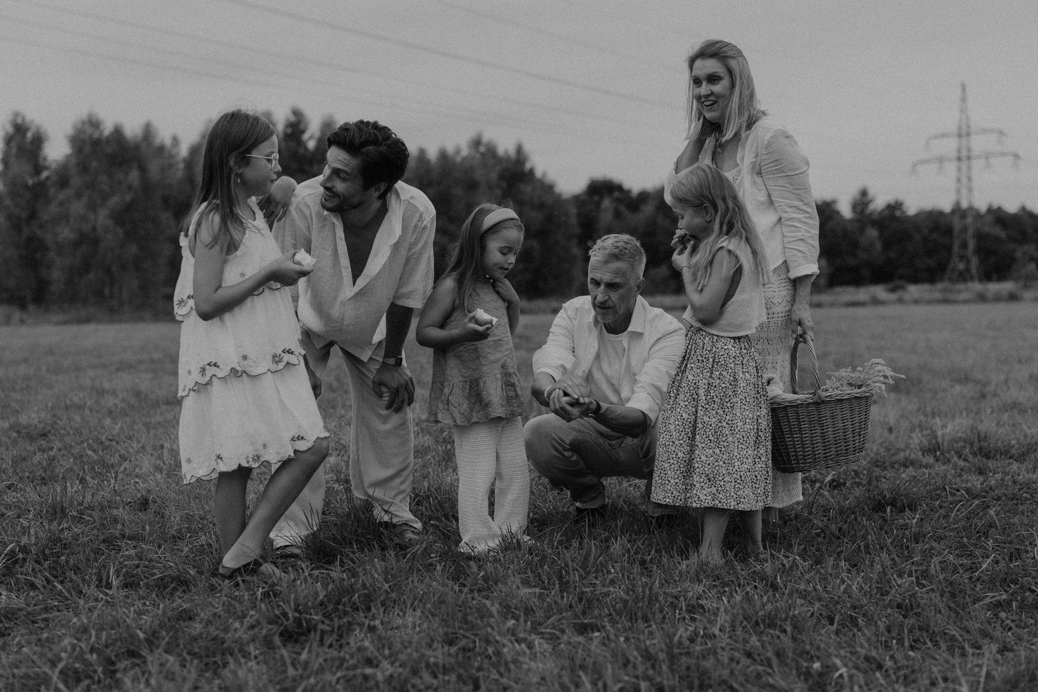 Black and white family photo of parents, grandparent, and three girls enjoying a picnic in a green meadow.