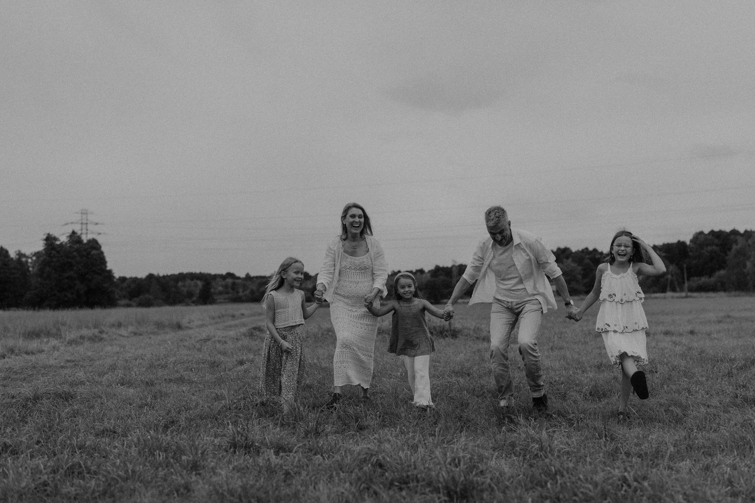 Black and white photo of a joyful family of five holding hands and running together in an open field.