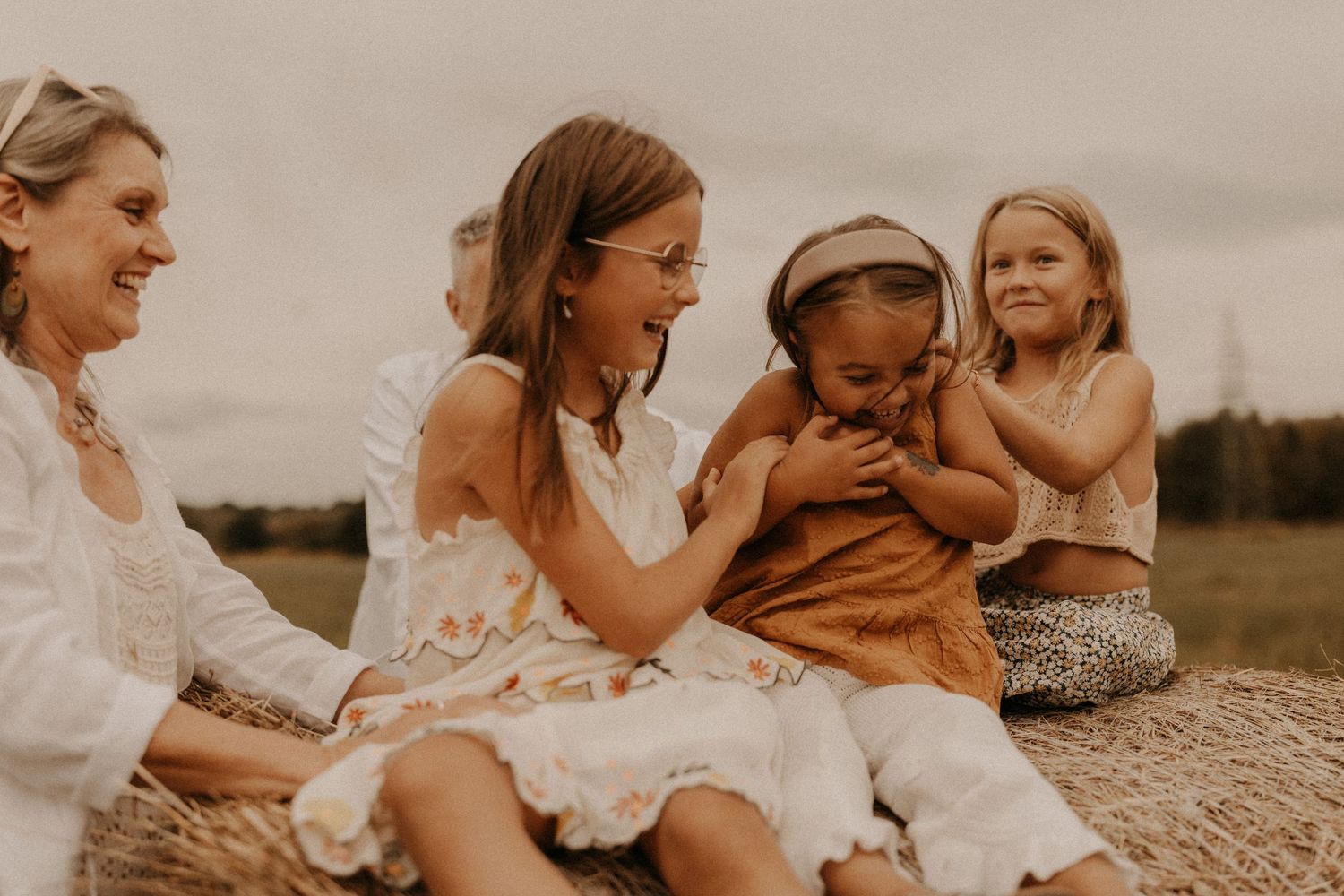 Women and girls laughing together on hay bales in a field, wearing boho summer dresses.