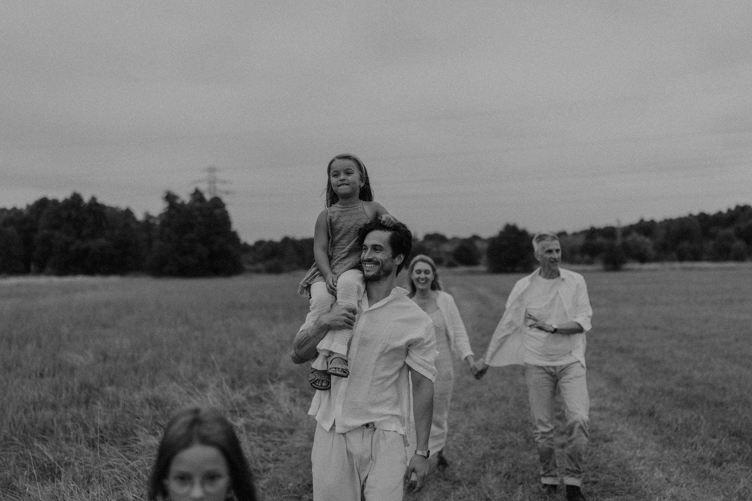 Black and white photo of a family walking through a field, with a child sitting on a man's shoulders.