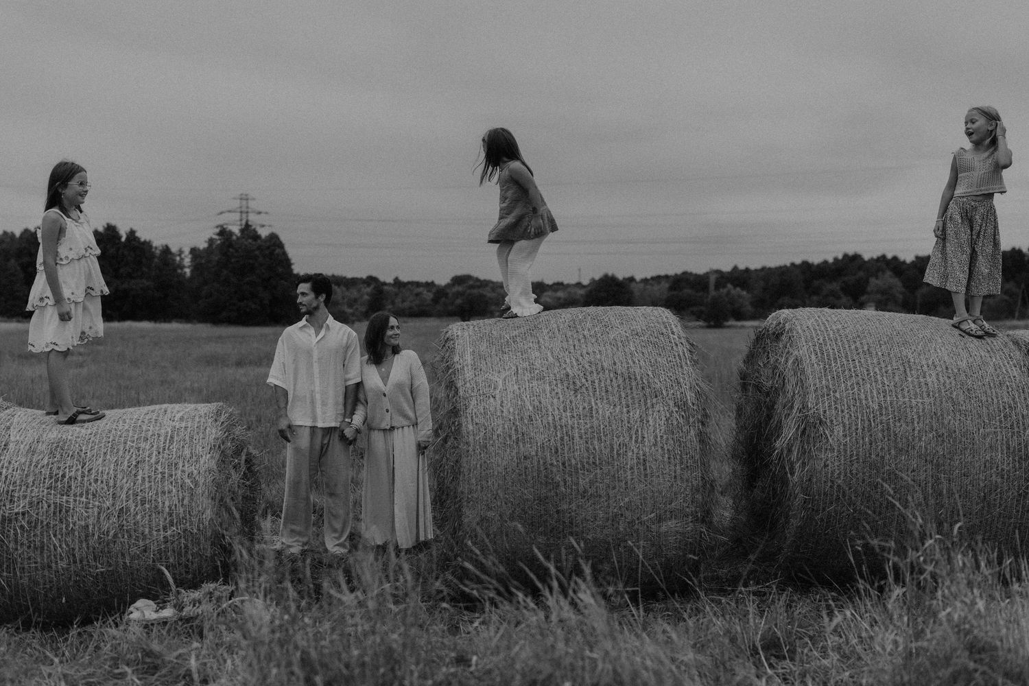 Black and white photo of a family posing among large hay bales in an open field on a cloudy day.