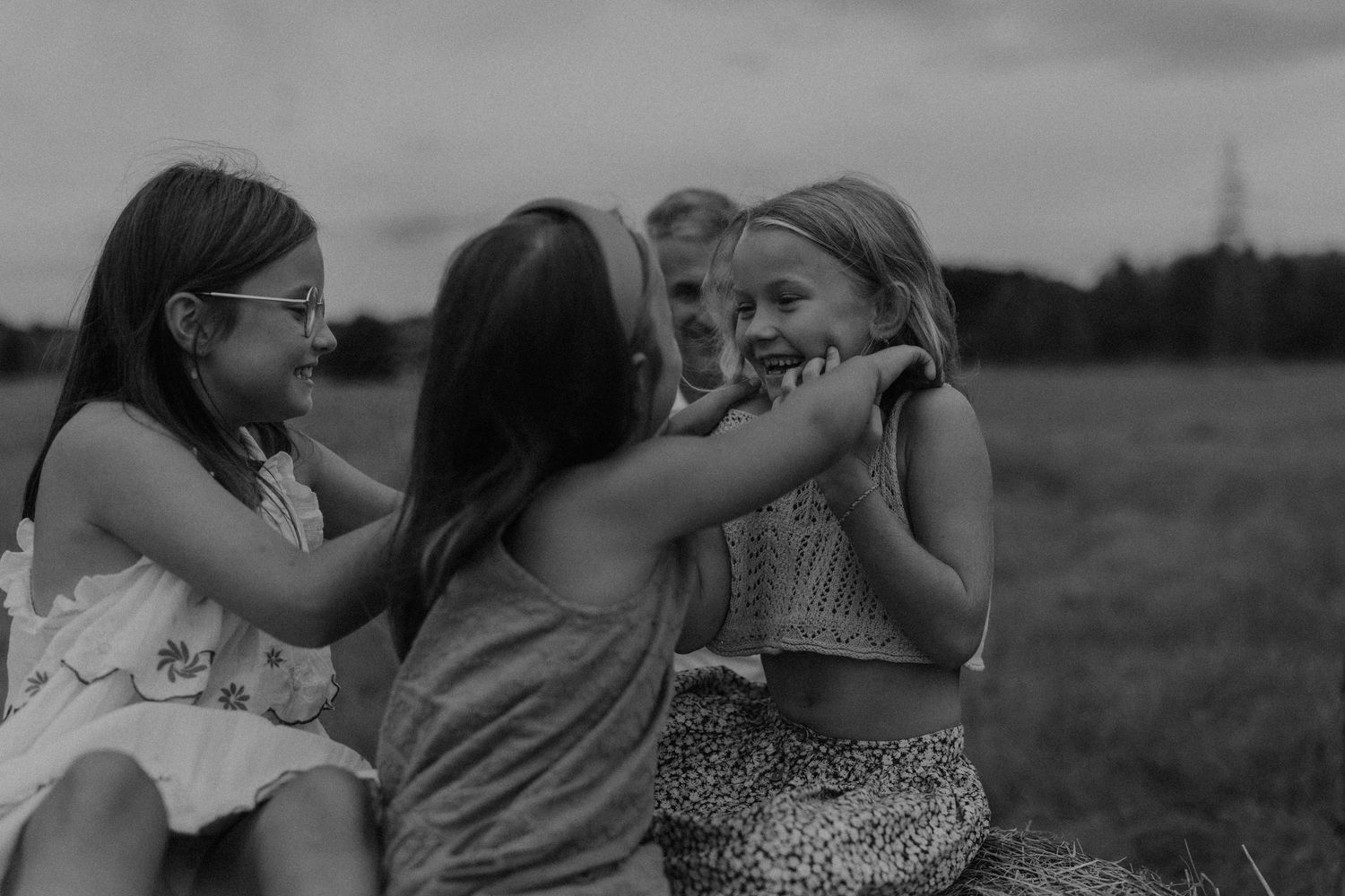 Black and white photo of four young girls laughing and playing together in an open field.