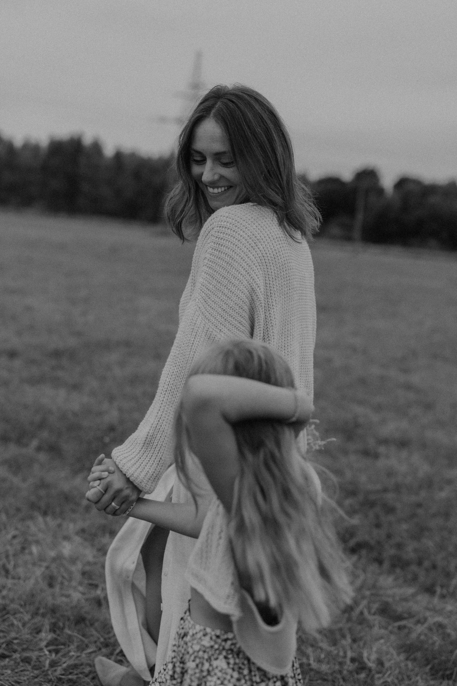 Black and white photo of a smiling woman holding hands with a young girl in an open field.