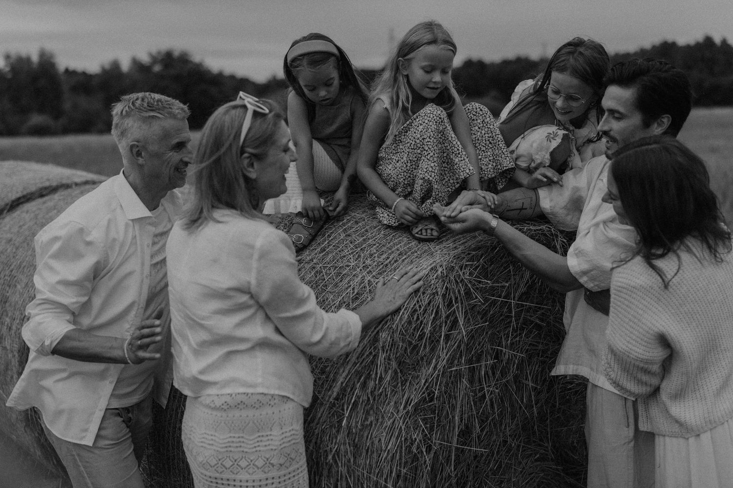 Black and white family photo gathered around a hay bale in a field, sharing a joyful moment together.