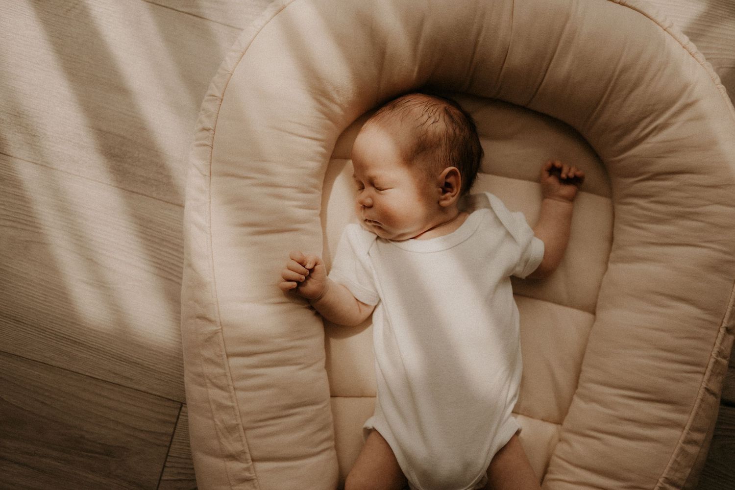 Overhead view of a sleeping newborn baby in a white onesie resting in a beige infant lounger. sesje zdjęciowe Rybnik, Wodzisław Śląski