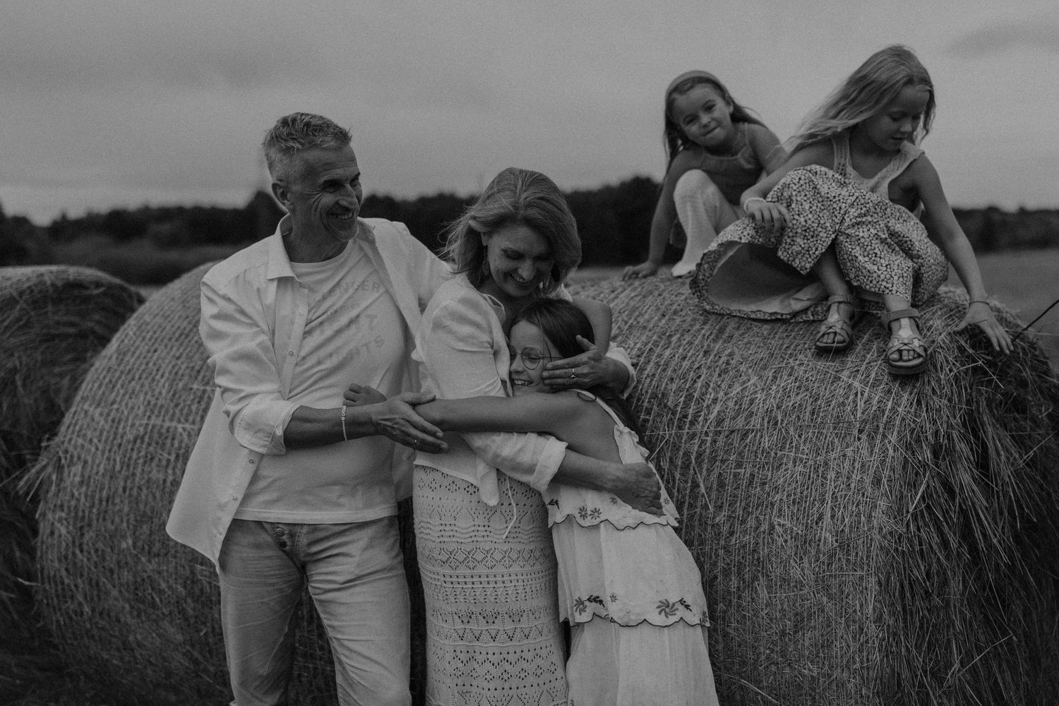 Black and white family photo with parents and children playing near large hay bales in an open field.