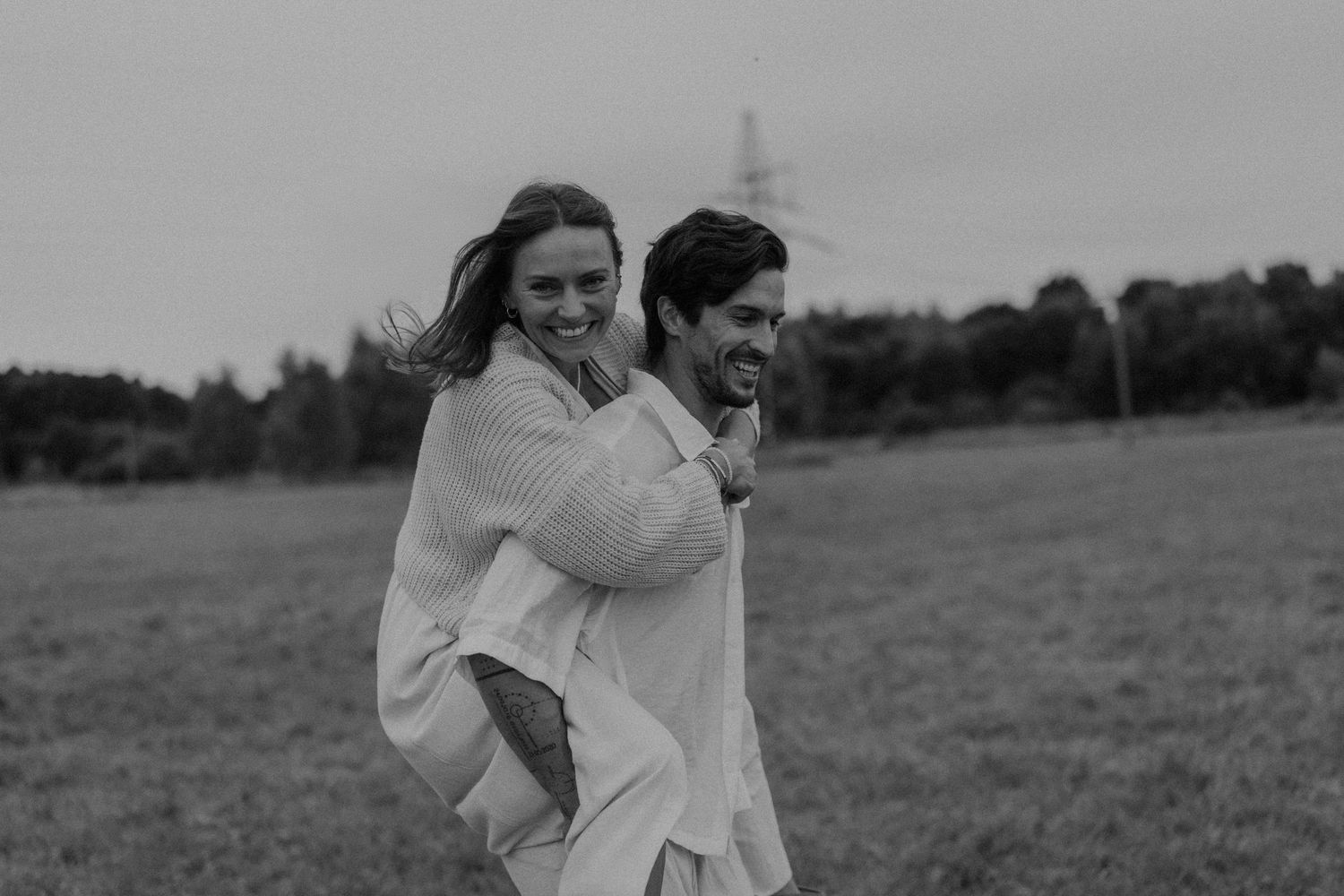A joyful couple shares a piggyback ride in a black and white photo on a lush green field.