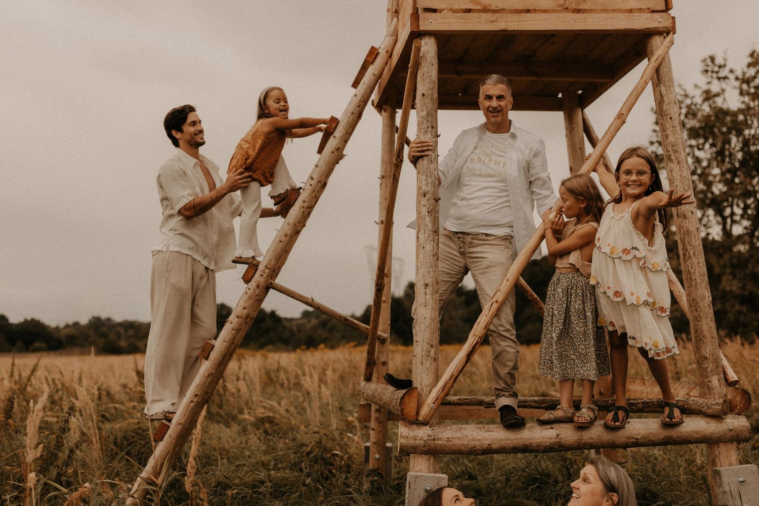 Family posing on a rustic wooden structure in a golden field during an outdoor photo session.