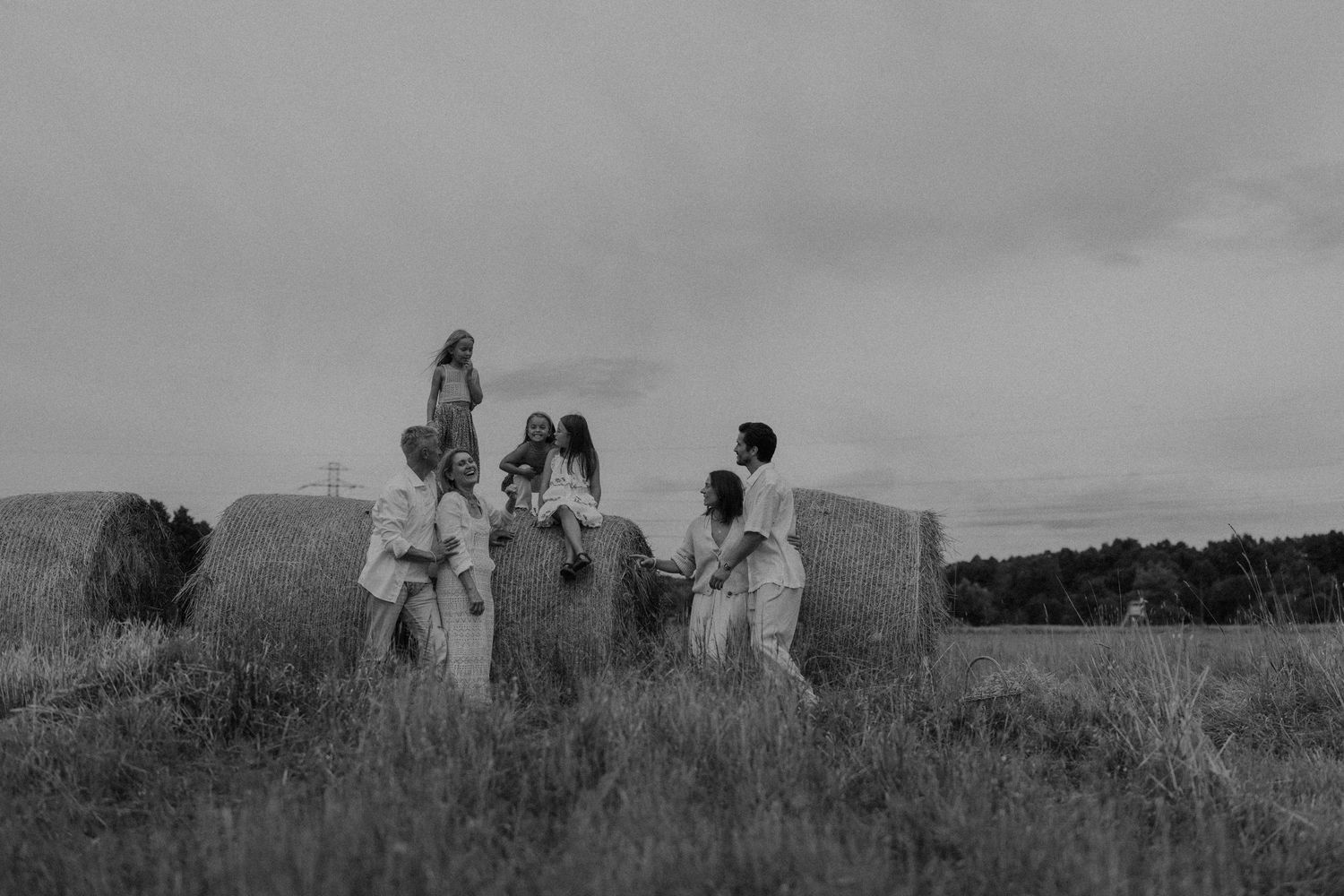 Black and white photo of a group of people gathered around large hay bales in an open field under cloudy skies.