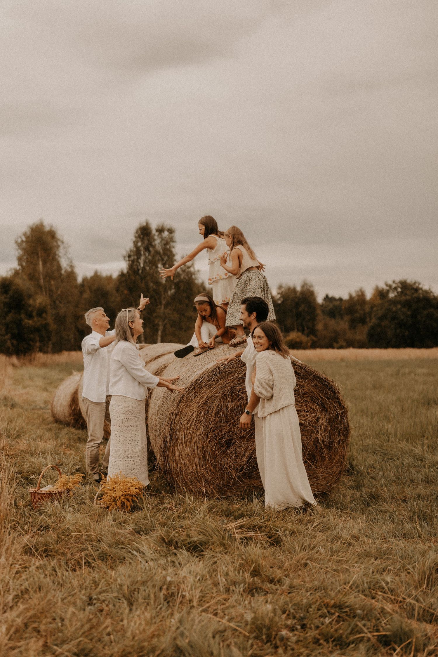 Group of friends posing around a large hay bale in an open field during a rustic outdoor photoshoot.