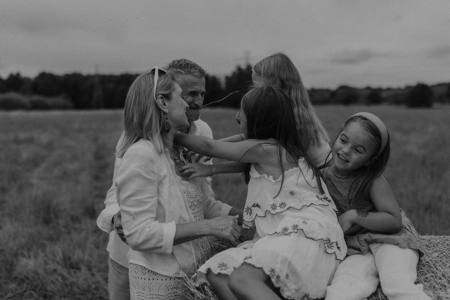 Black and white family photo of parents and two girls laughing together in a field.