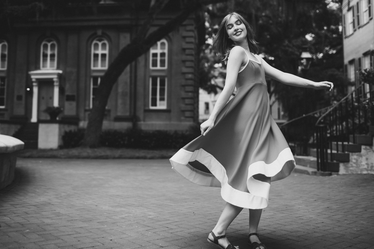 Black and white portrait of a girl twirling in a flowing dress in a brick courtyard, Cistern, Charleston SC