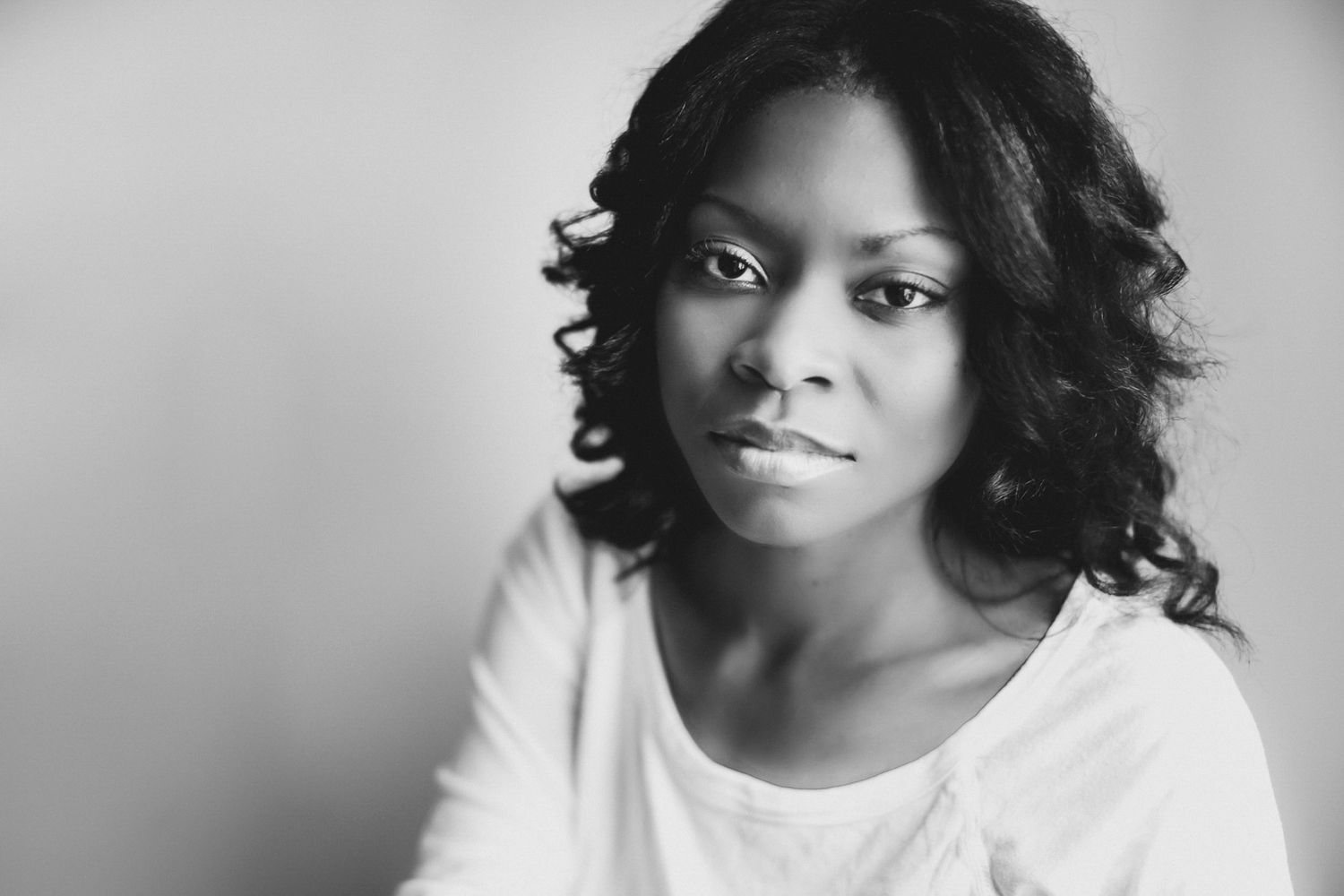 Black and white portrait of a woman with dark curly hair and a calm, confident gaze, wearing a white top
