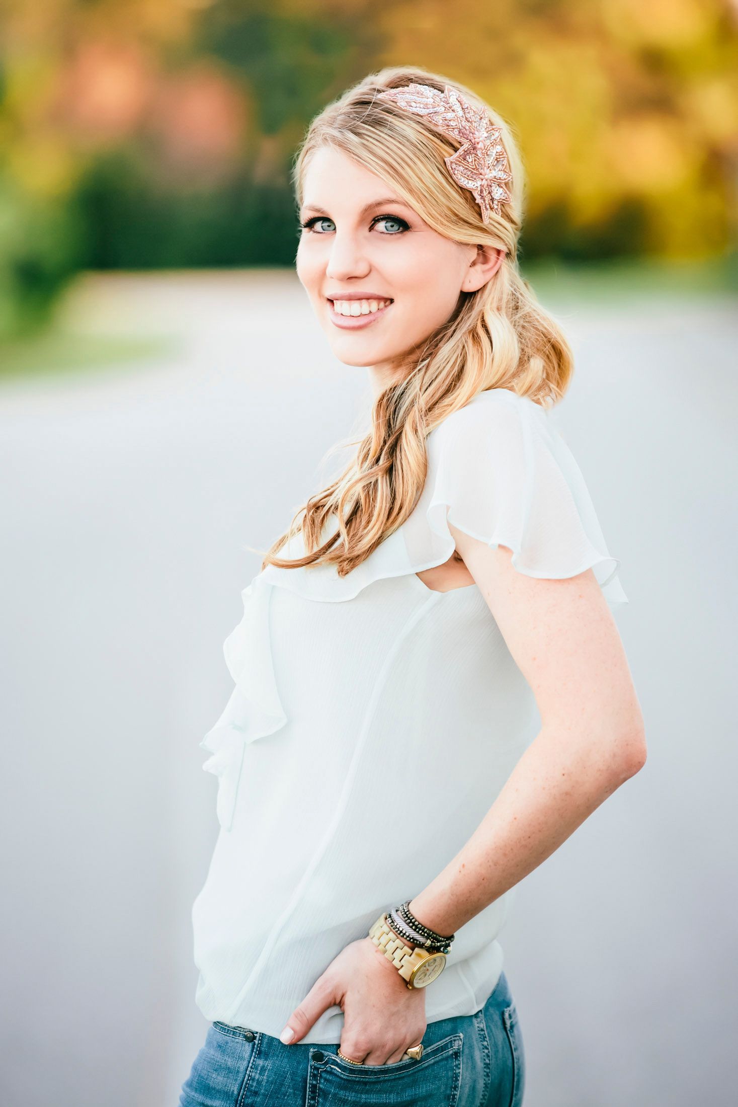 Smiling woman with a long side ponytail and a patterned headband, hand in her jeans pocket, in warm golden light