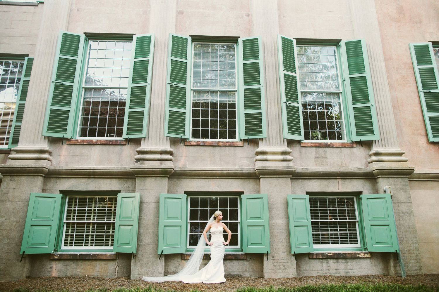 Bride in a veil standing in front of a historic building with green shuttered windows