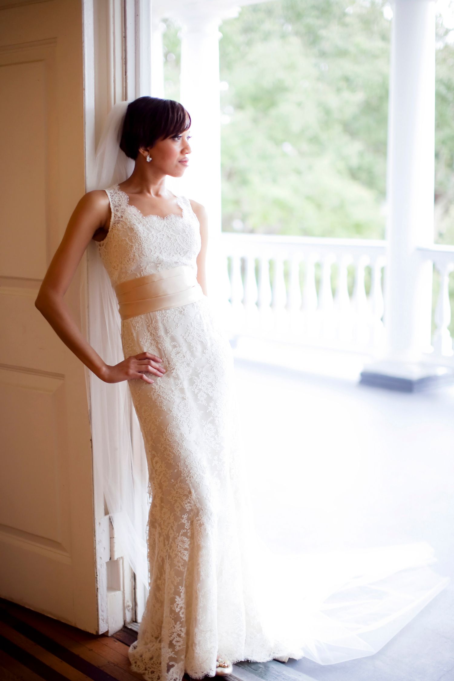 Woman in a lace gown with a veil standing in a doorway beside a columned porch, light streaming in, Lowndes Grove Plantation