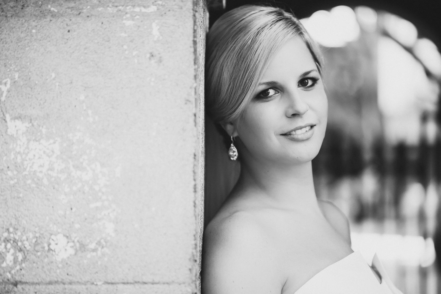 Black and white portrait of a woman with elegant drop earrings resting against a textured stone wall