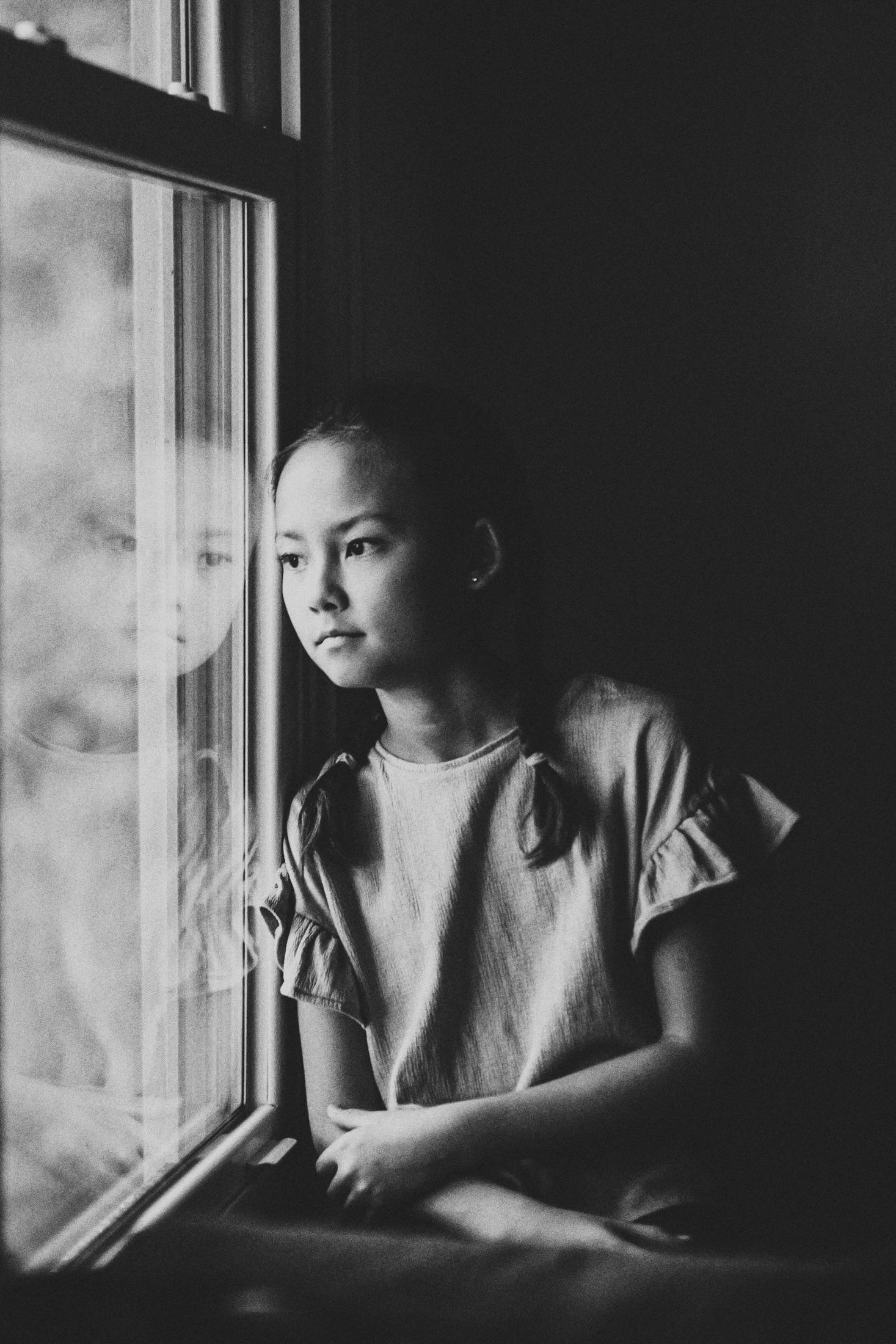 Black and white image of little girl gazing out the window