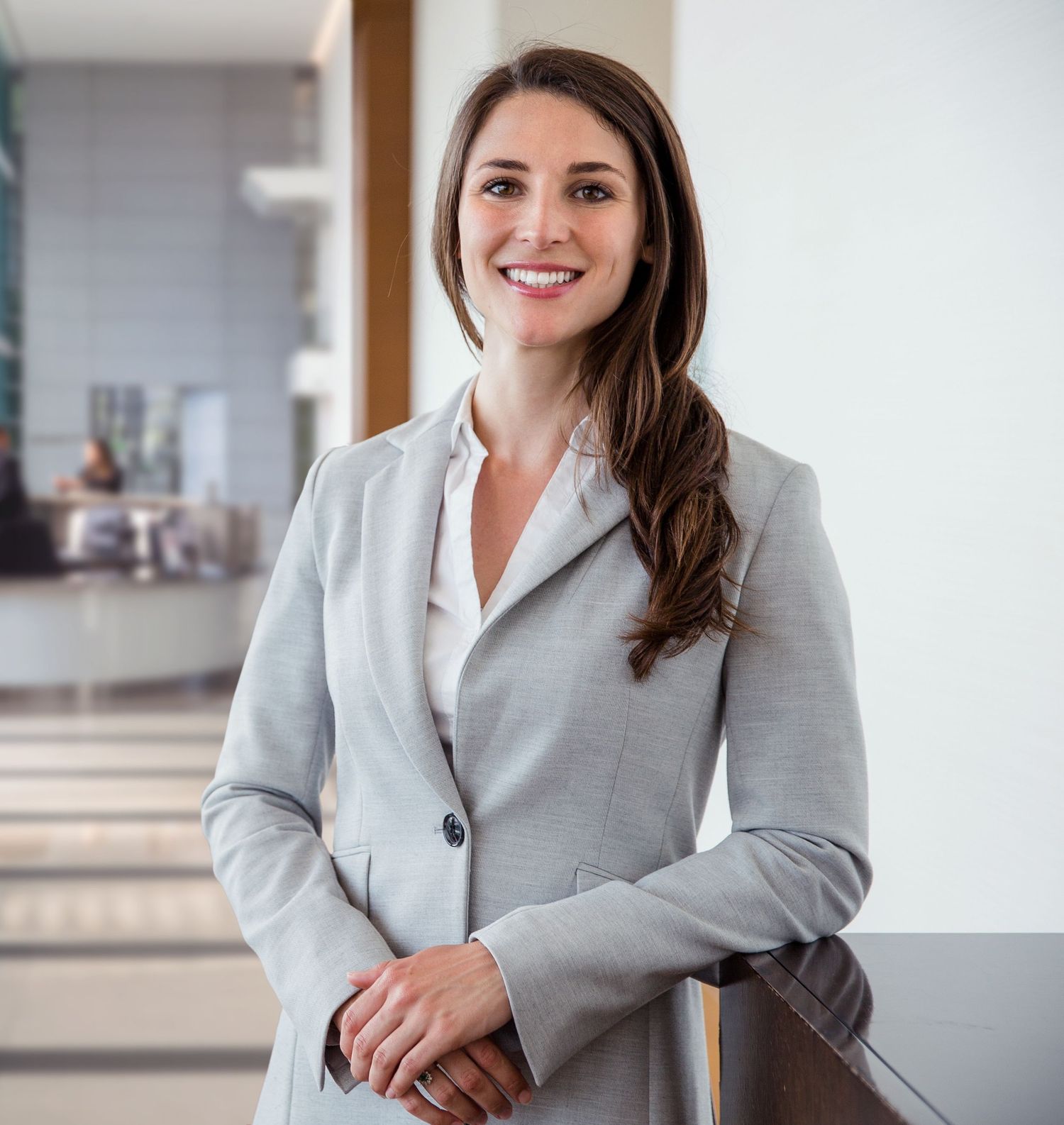 Professional businesswoman in gray blazer smiling confidently in modern office lobby.
