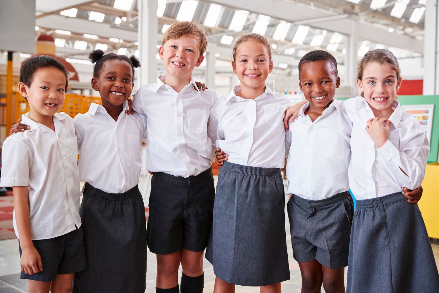 Six diverse school children in uniforms smiling together in a gymnasium.