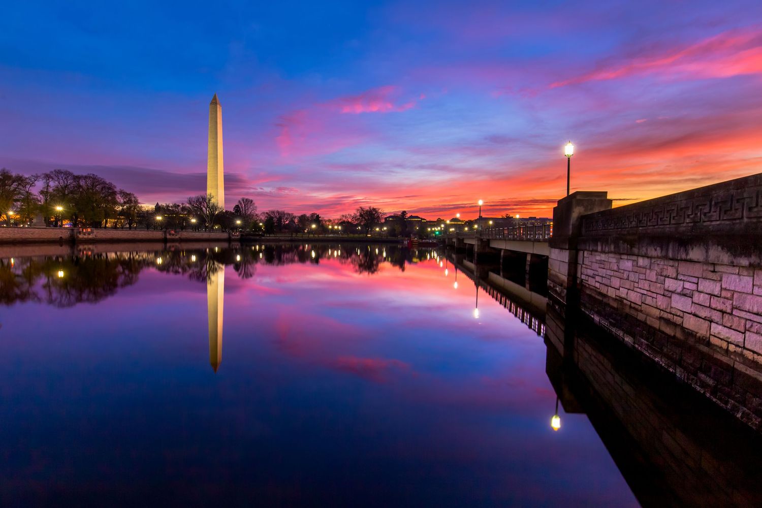 Washington Monument reflected in calm Tidal Basin waters at dramatic pink and blue sunset in Washington DC.