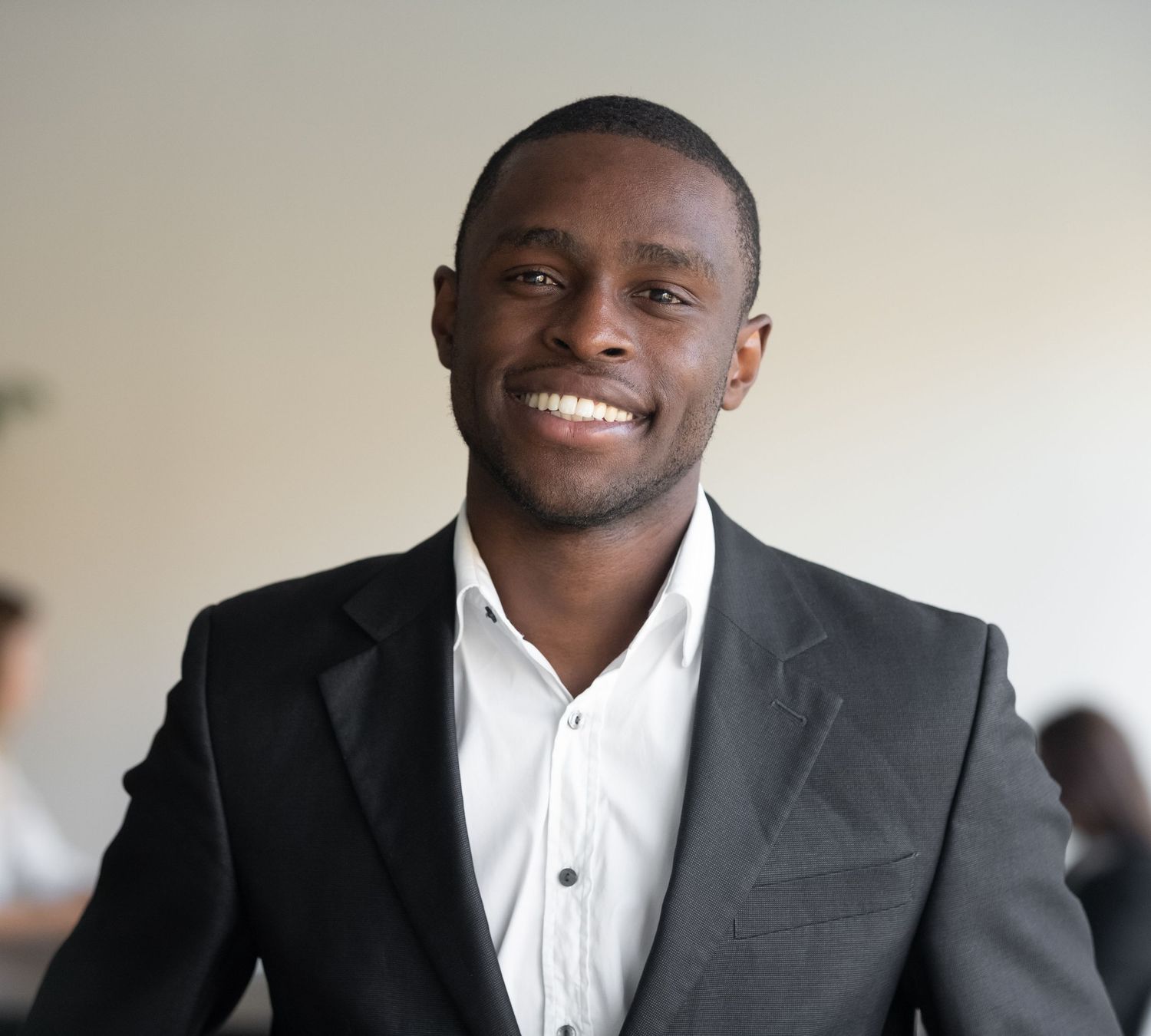 Smiling young Black businessman in black suit and white dress shirt posing confidently in a bright modern office.