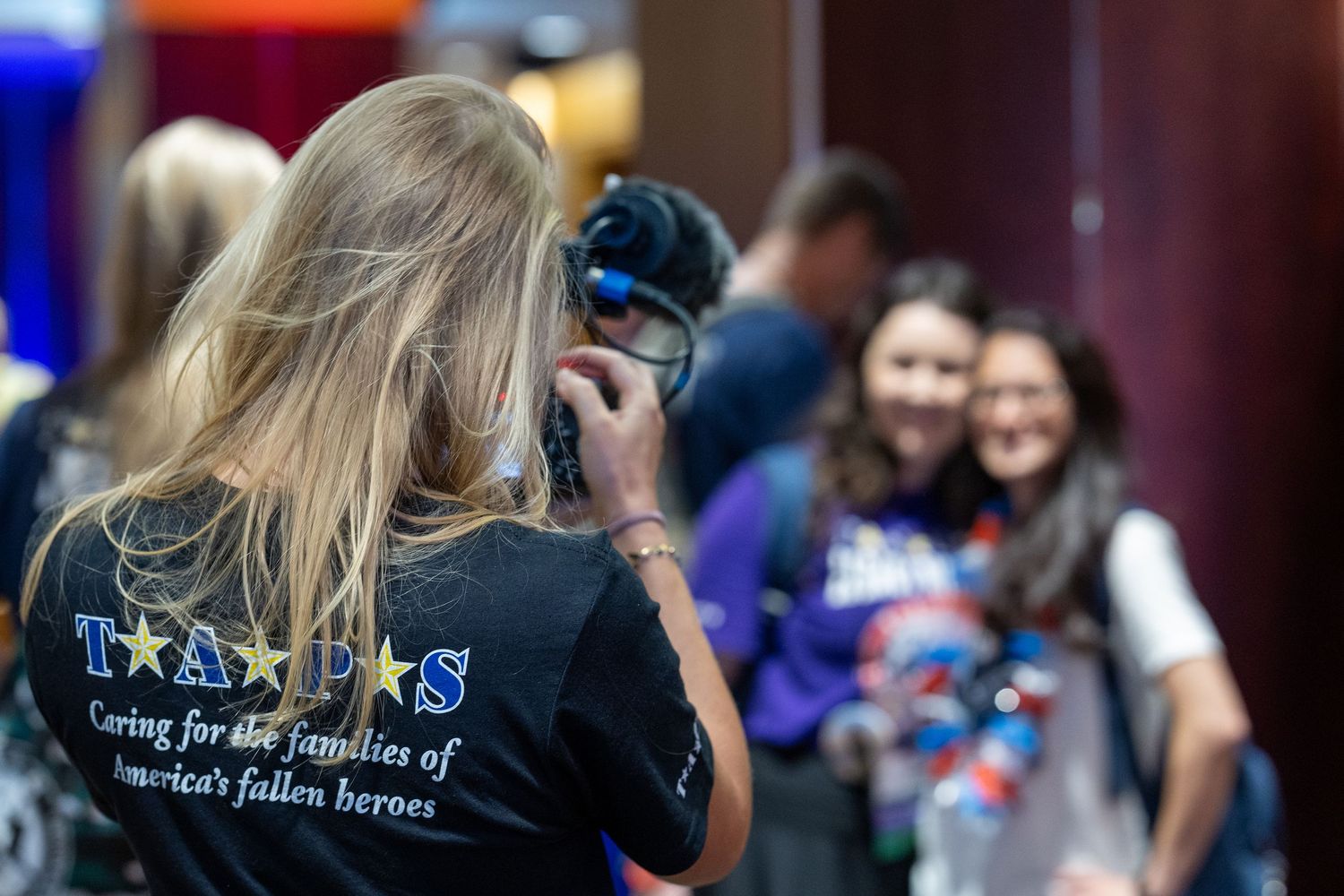 A photographer wearing a TAPS shirt captures smiling attendees at a memorial event honoring fallen military heroes.