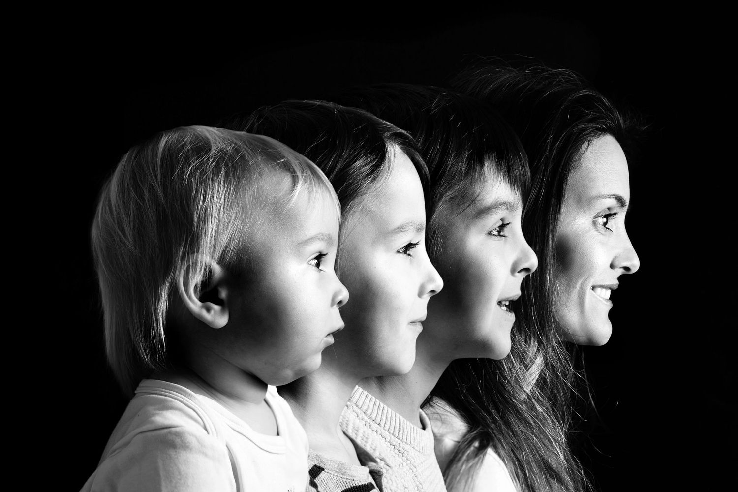 Black and white profile portrait of a mother and her three children lined up by age, showing family growth.
