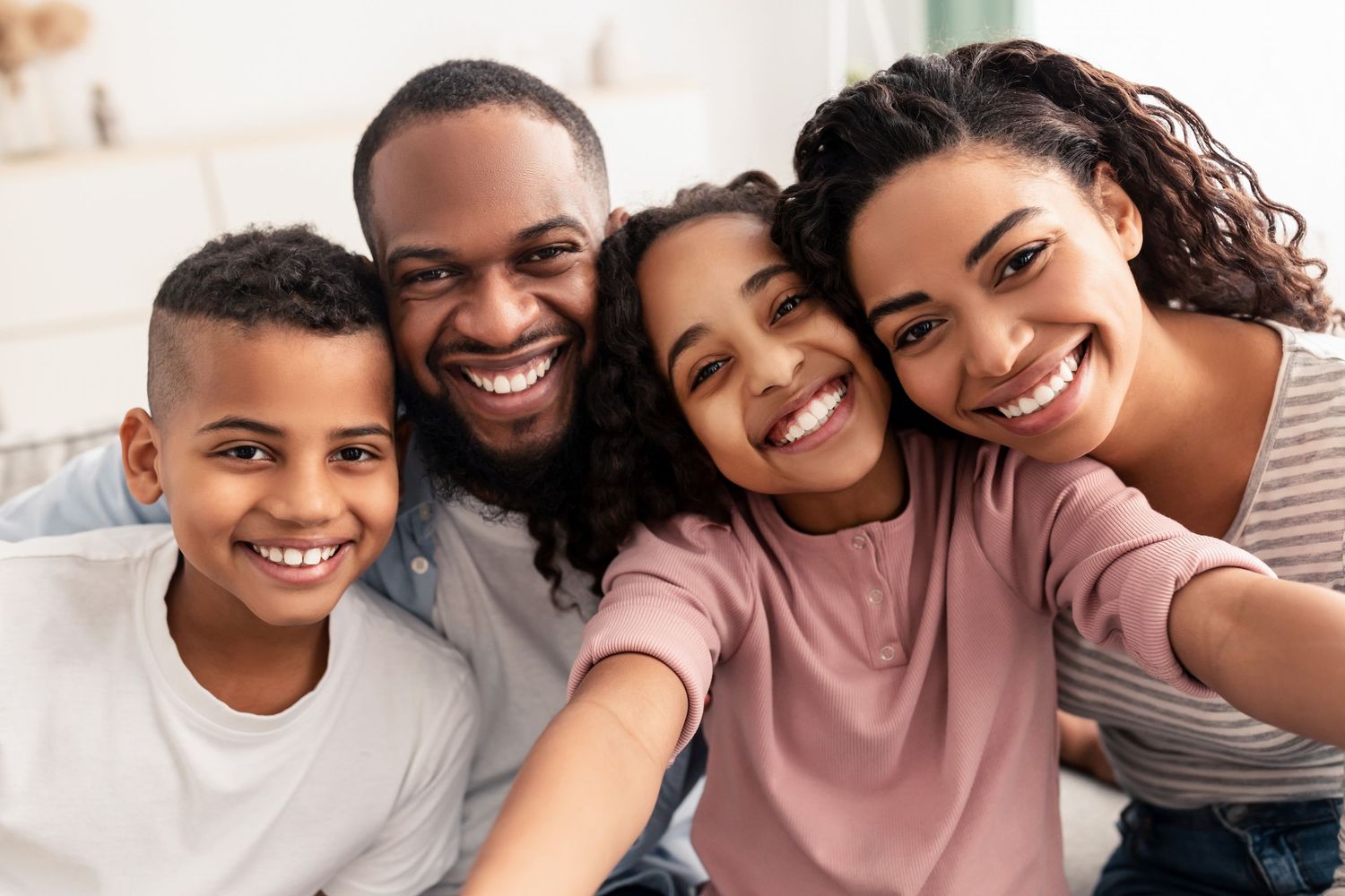 Happy Black family of four smiling together in a bright indoor selfie portrait.