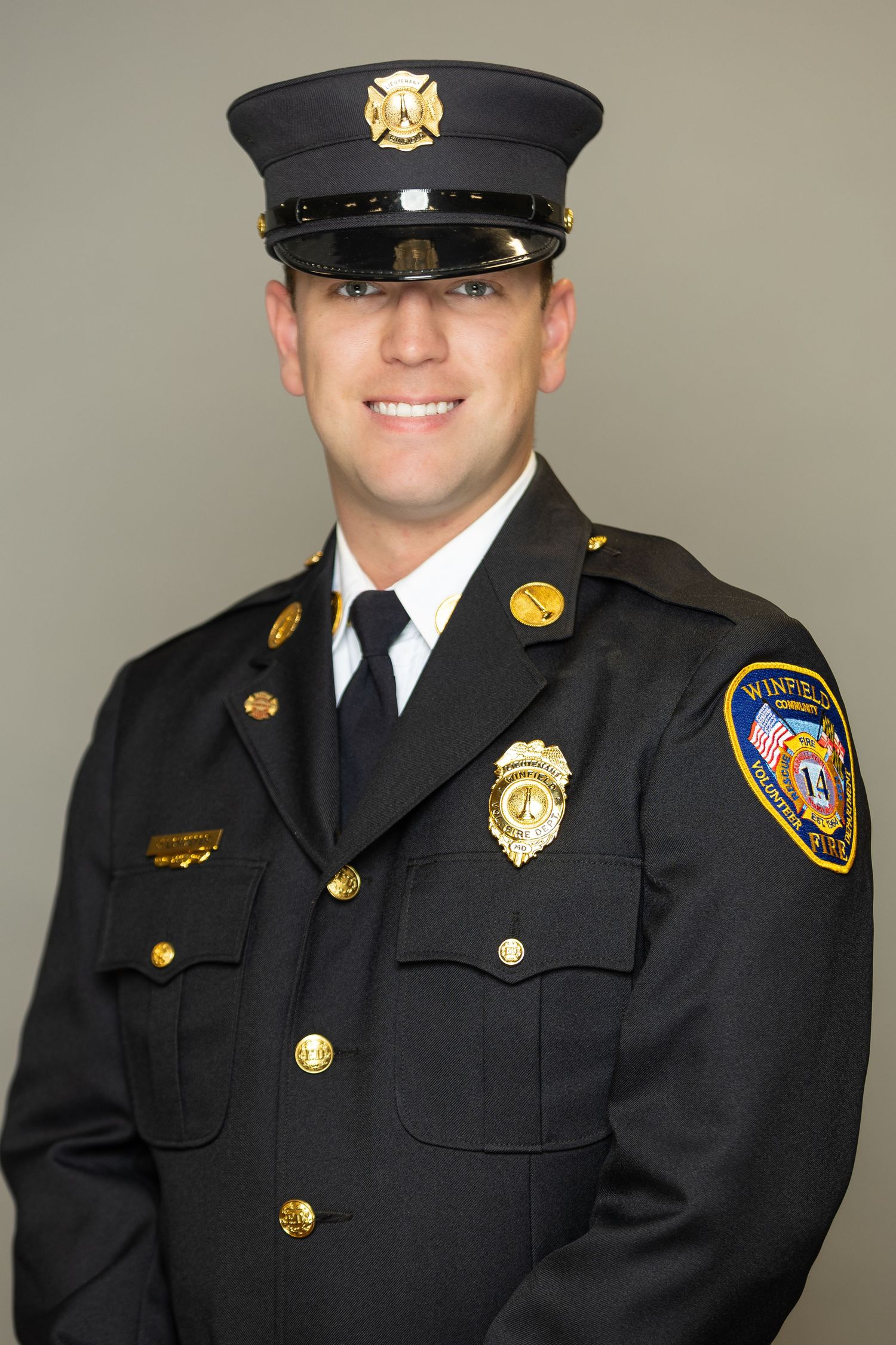 Smiling firefighter in black dress uniform with badge and Winfield Fire Department patch poses for official portrait.