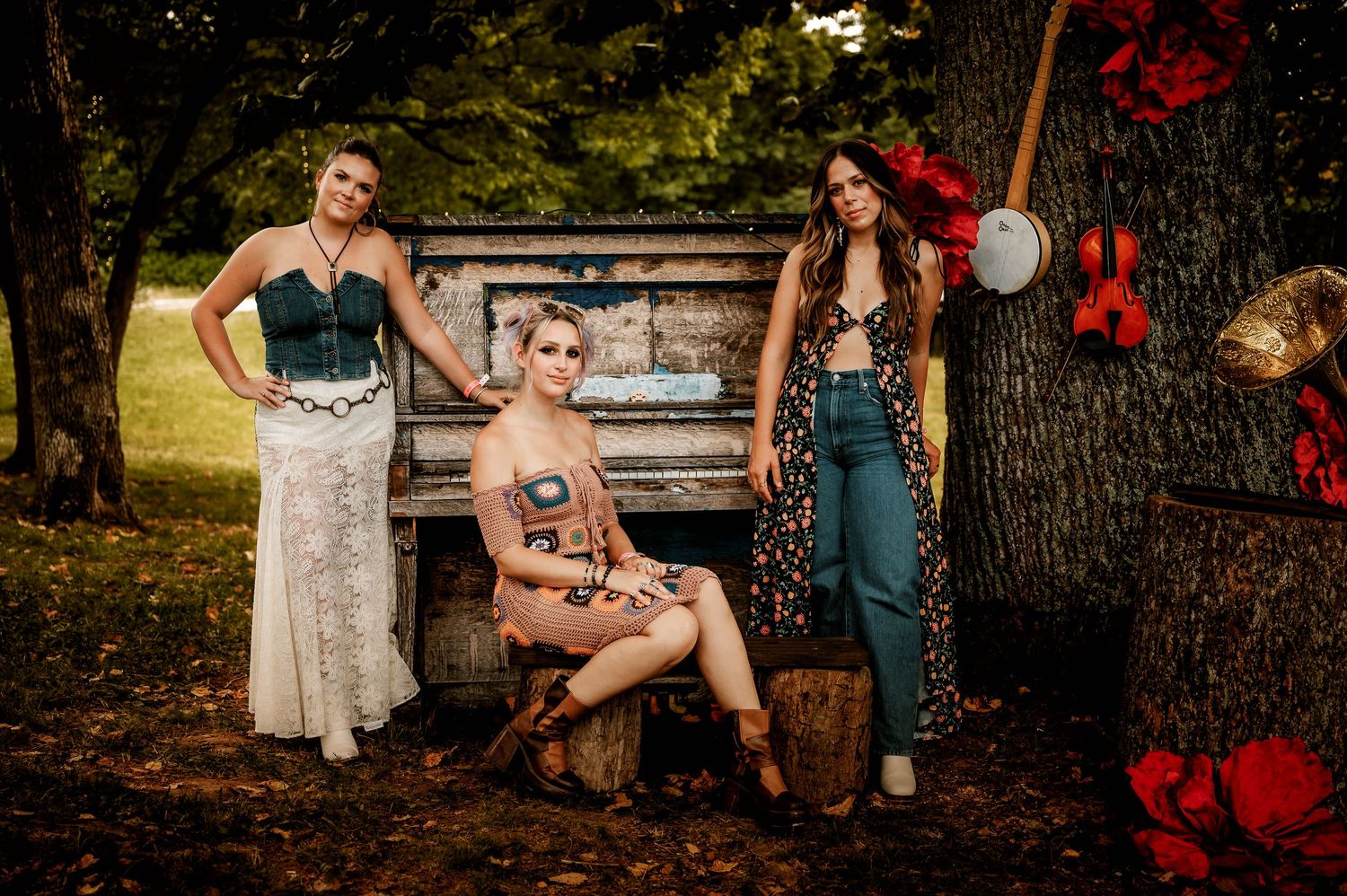 A rustic outdoor photo shoot featuring three people posing in vintage style clothing by an antique piano.